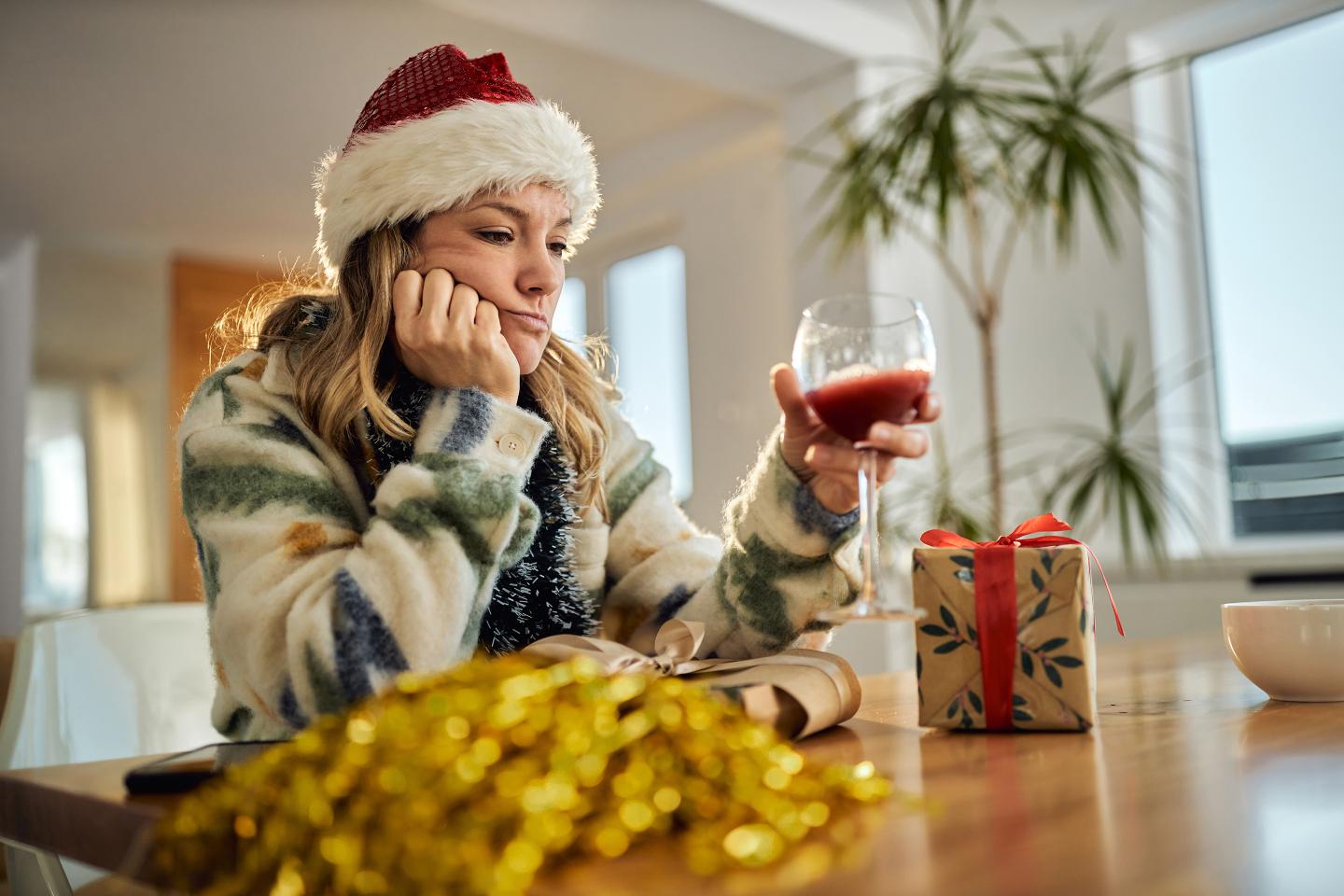 Depressed woman in Santa hat drinking wine alone.