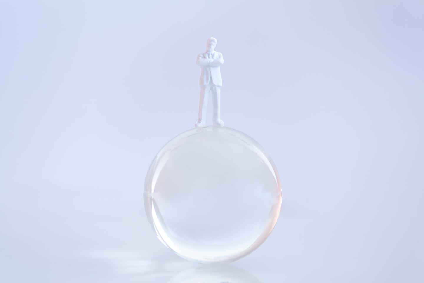 Man (white figure) balancing on a crystal ball.