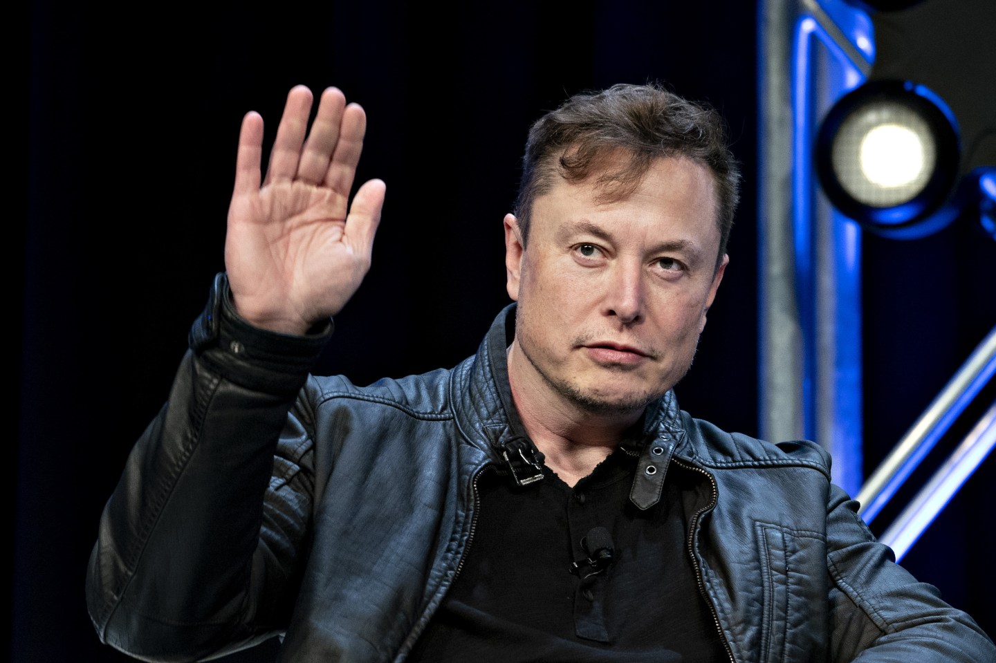 Twitter CEO Elon Musk waving, wearing a black leather jacket and tshirt.