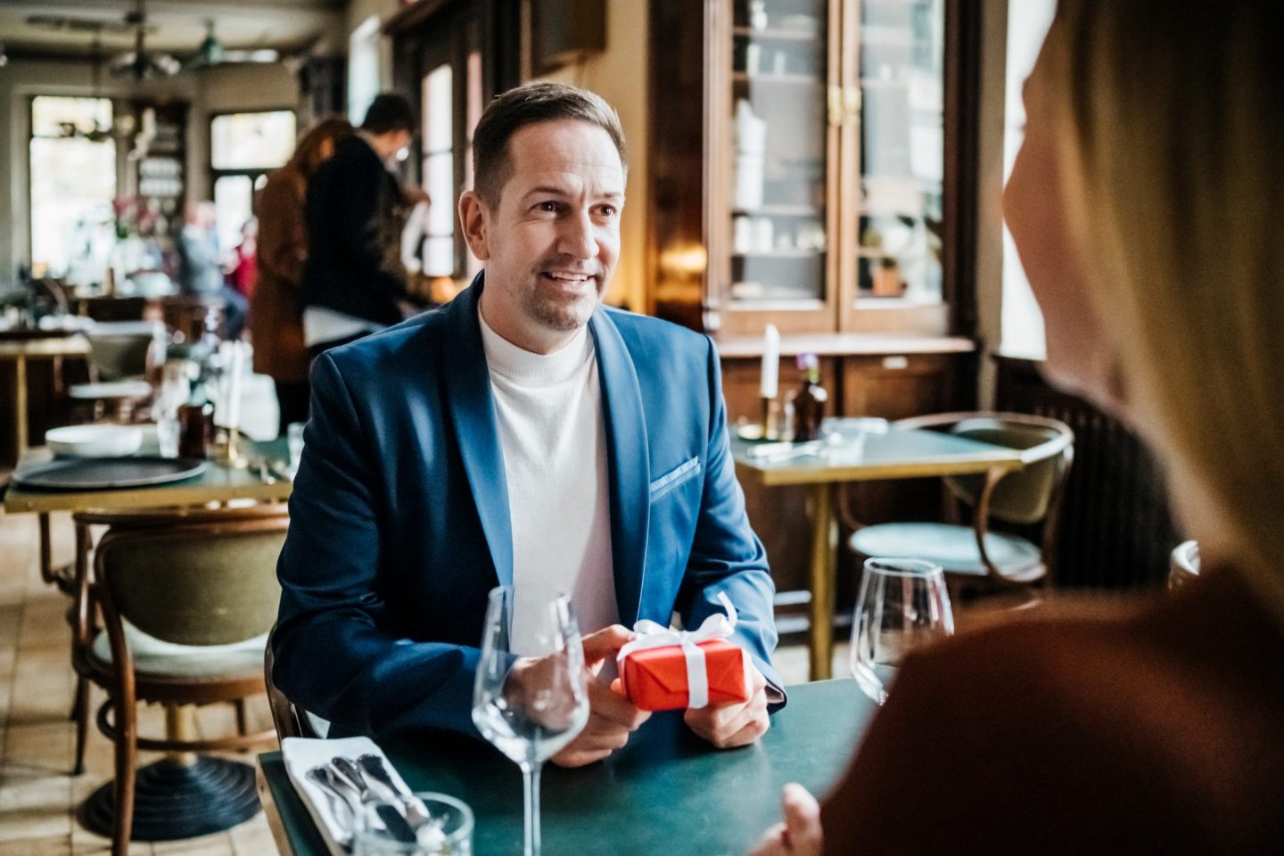 Man smiling as he is about to give partner a small gift in a restaurant