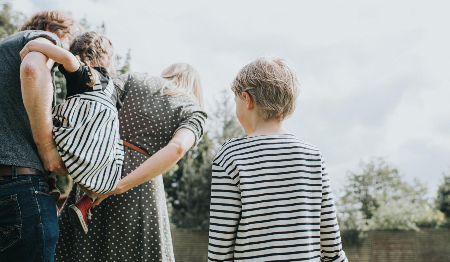 Young boy standing back and watching a family