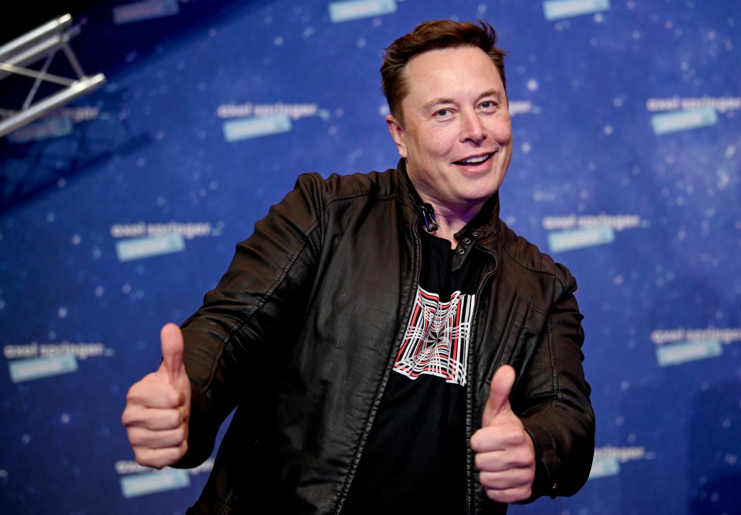 Elon Musk smiling and with both thumbs up while on stage