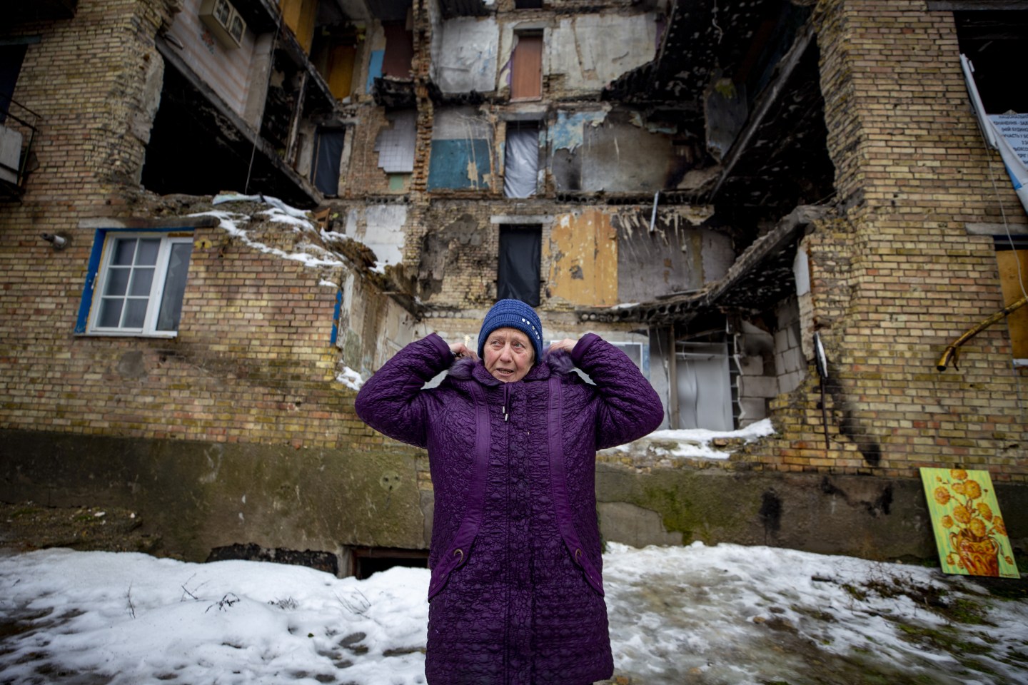 A woman standing alone in front of a bombed out building.