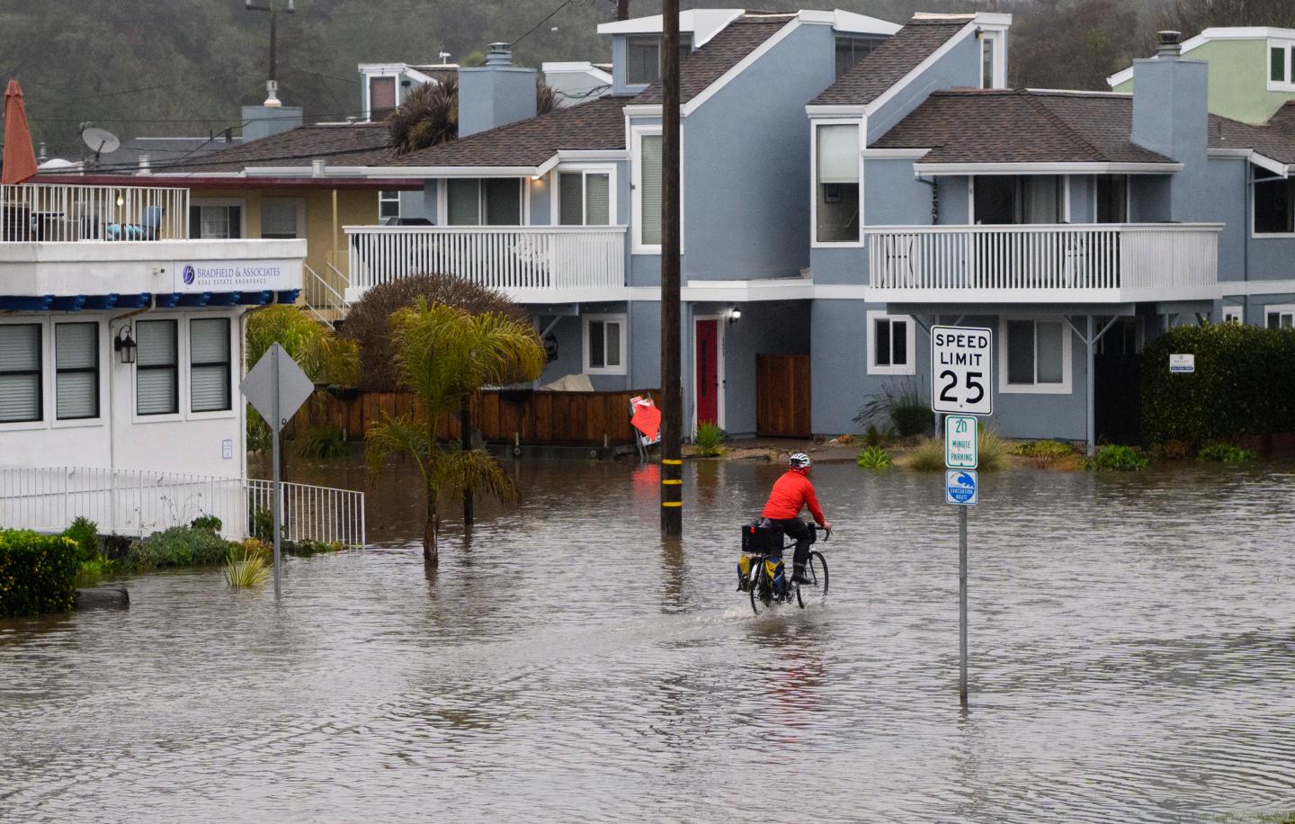 A man rides his bike through a flooded road in Aptos, California.