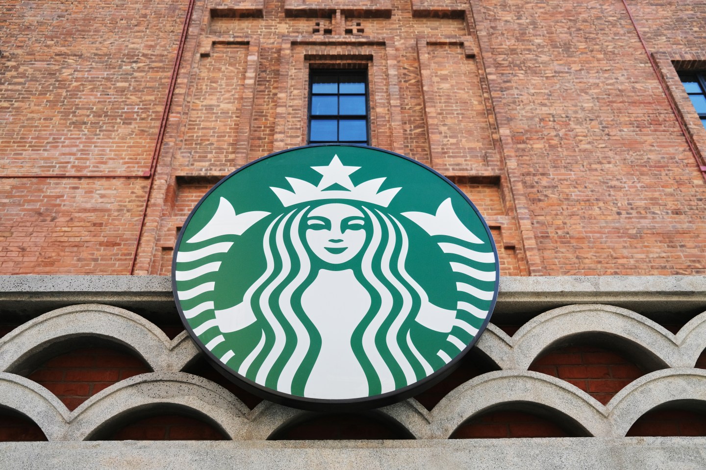 Logo of Starbucks hangs on the well kept brick-wall of the old building.