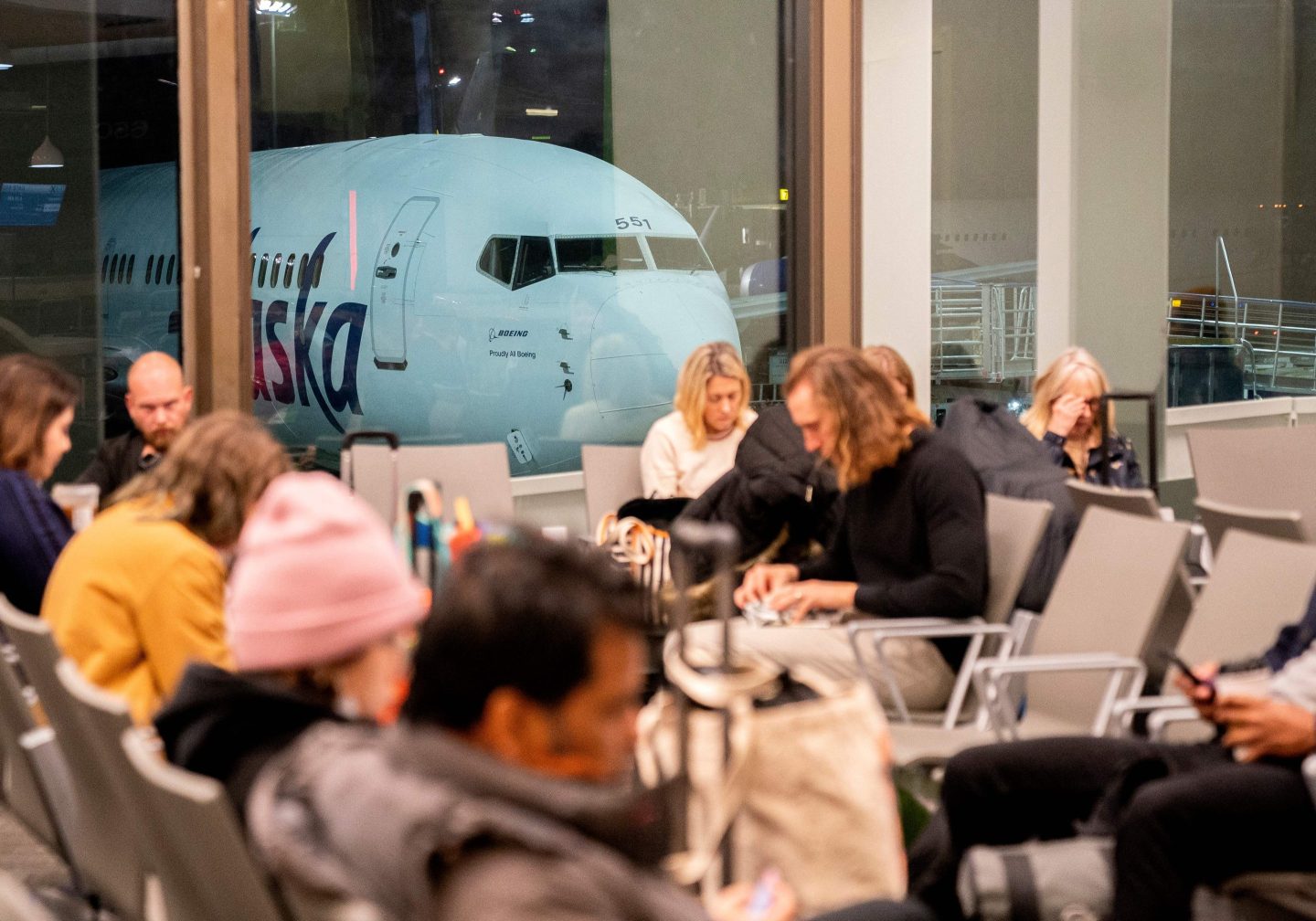 Travelers wait in the terminal as an Alaska Airlines plane sits at a gate at Los Angeles International Airport in Los Angeles
