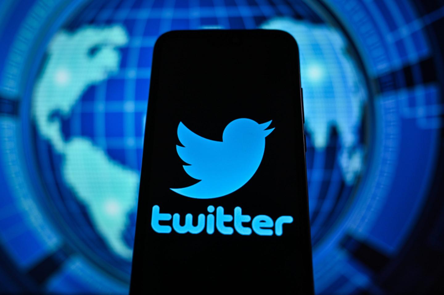 Twitter logo is displayed on a smartphone with graphics world map on the background.