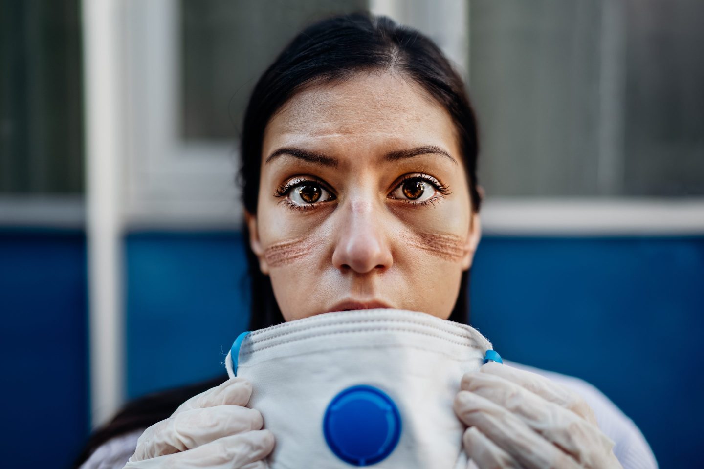 A tired-looking medical worker removes her mask