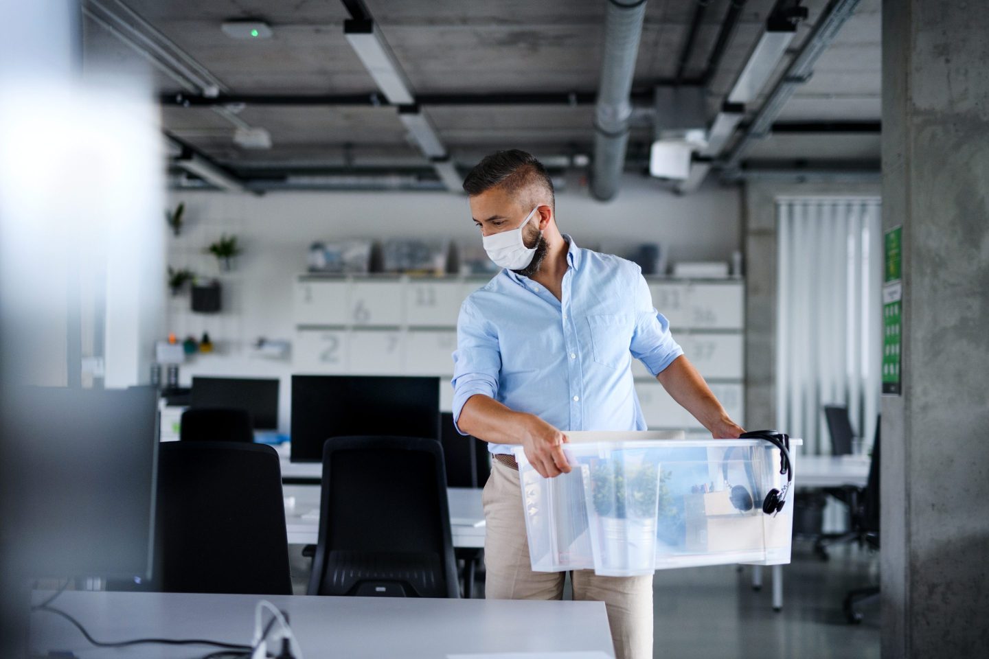 Mature man with face mask standing at desk, leaving office.