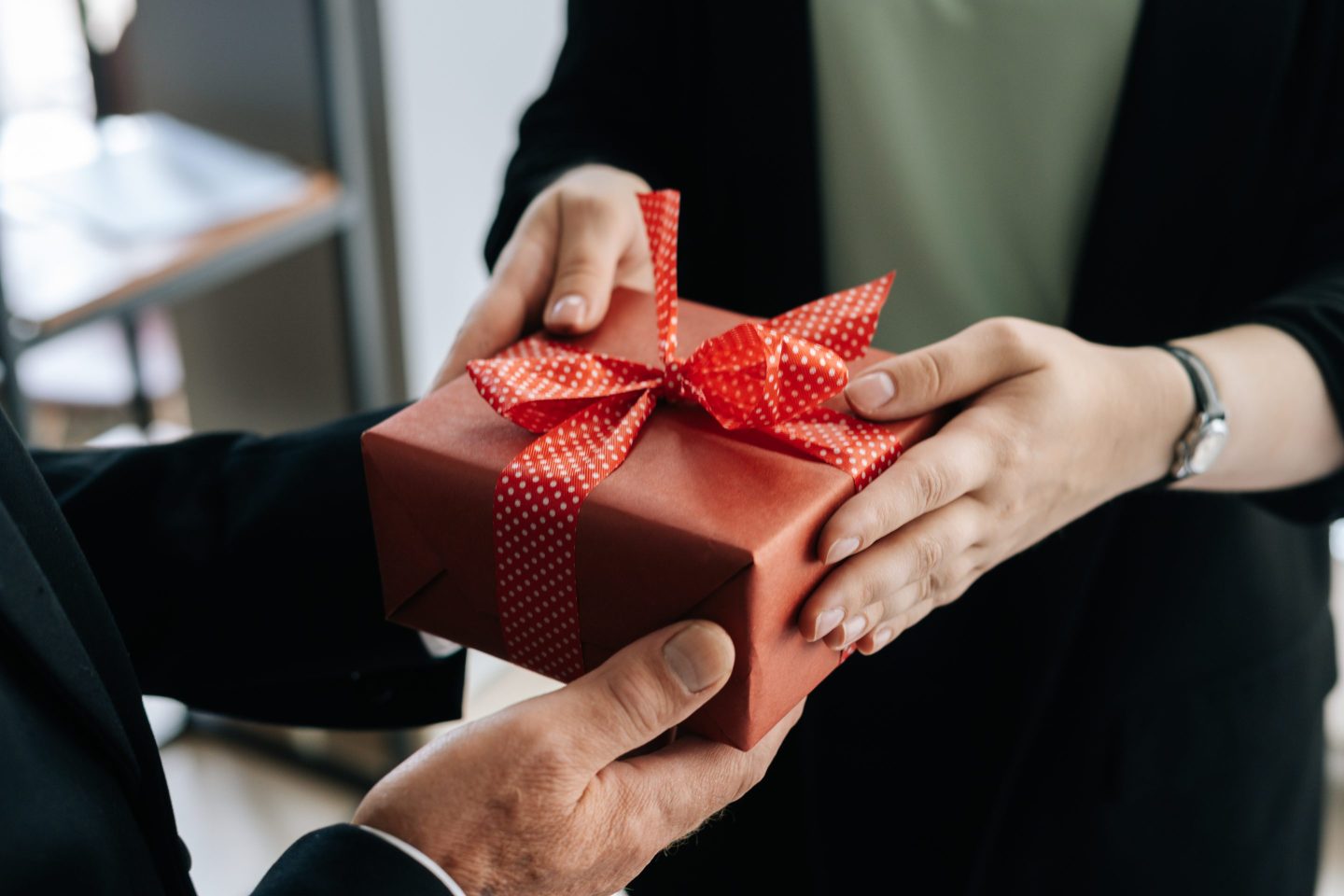 Close-up view of hands of unrecognizable woman giving red gift box tied to bow handed to man