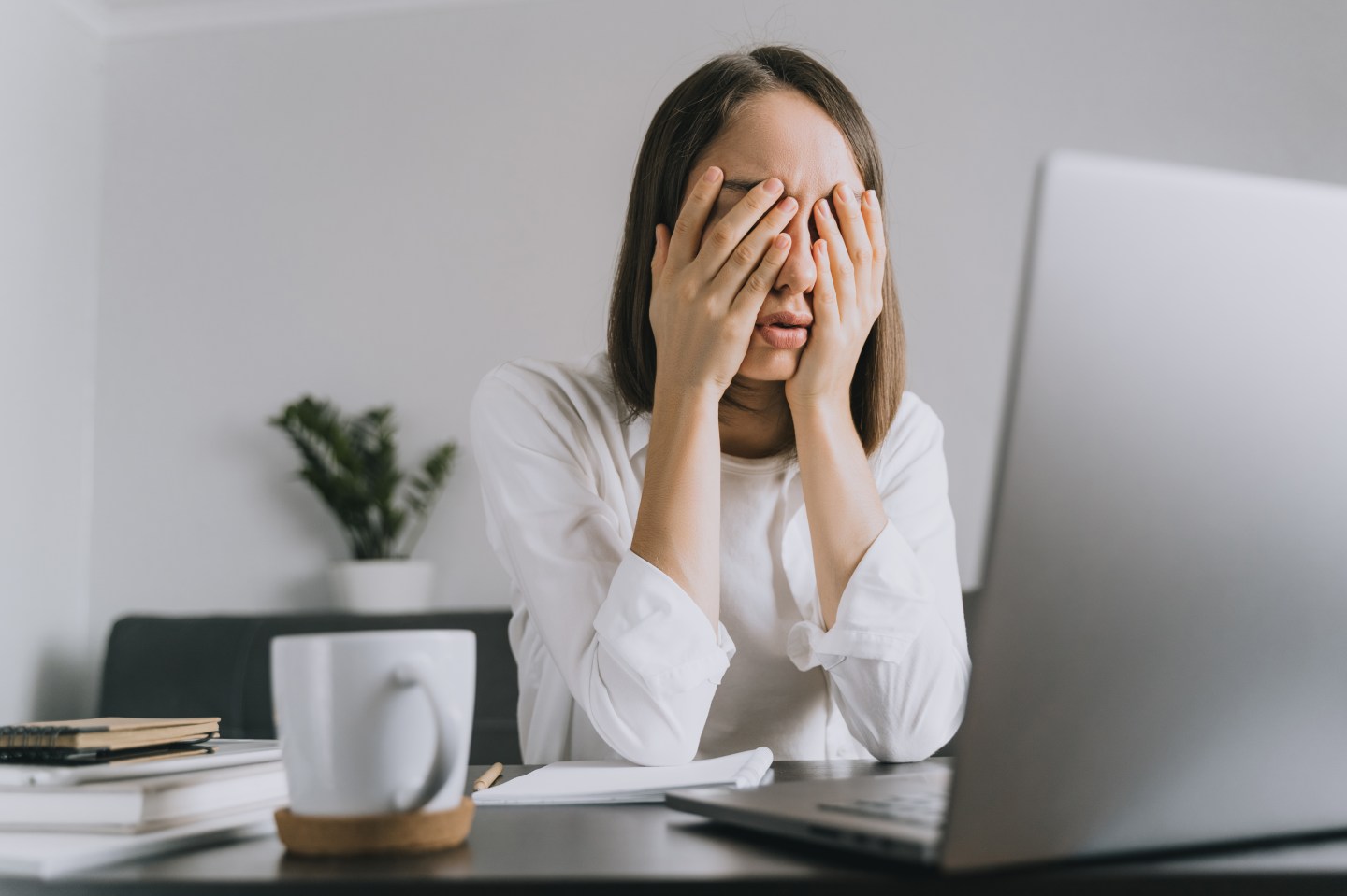 A woman with her hands over her face who is working in a home office.