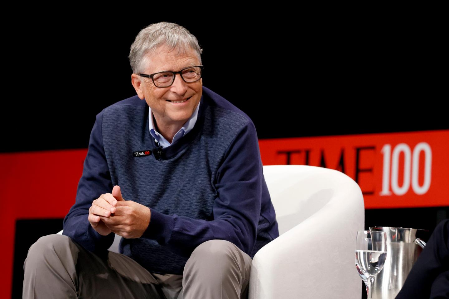 Bill Gates sitting on an armchair and smiling on-stage during a summit