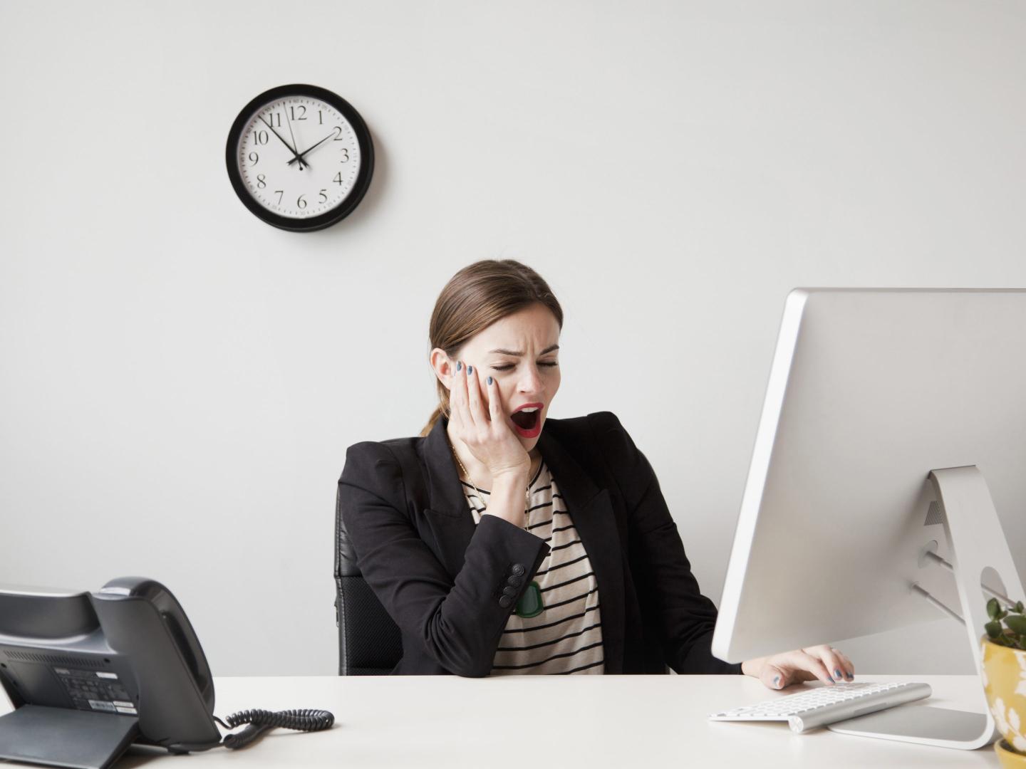 Young businesswoman yawning and looking bored in front of her computer in an office