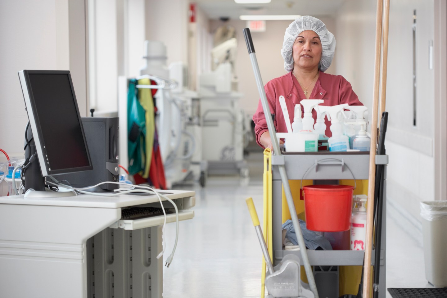 A cleaning woman pushing a cart through a hospital corridor