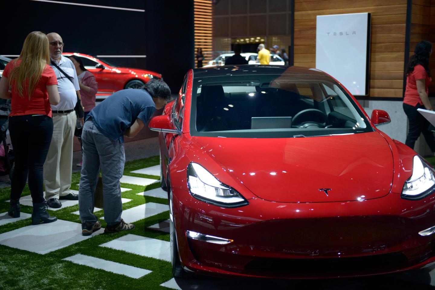 People inspect the Tesla Model 3 as it sits on display at the Los Angeles Auto Show.