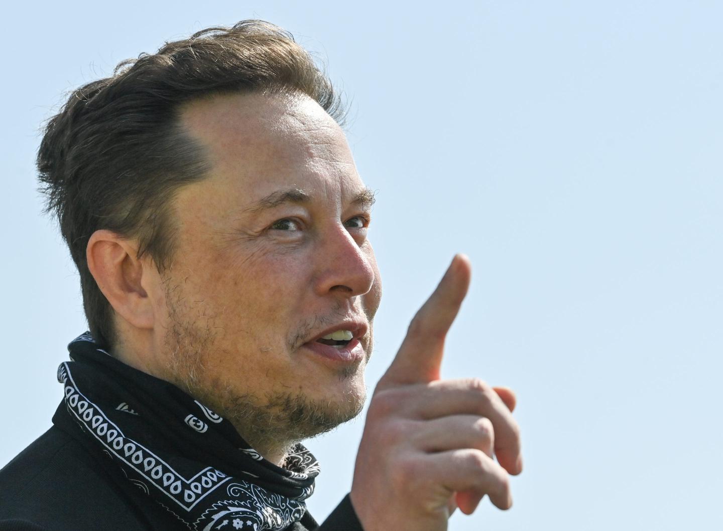 Elon Musk smiles and points to an unseen person.