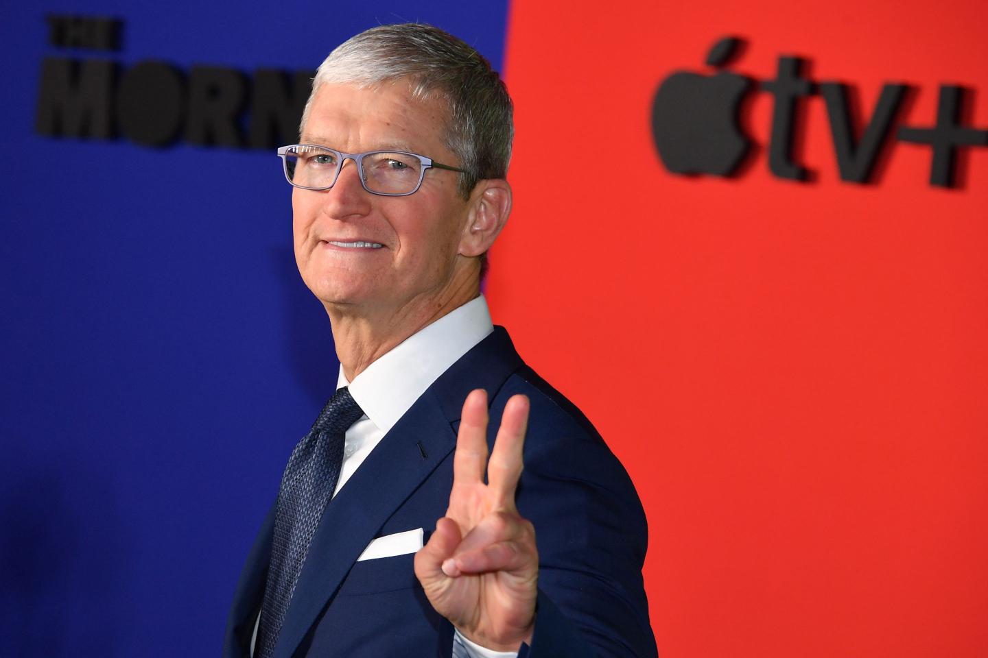Apple CEO Tim Cook smiles and makes a peace sign for press photographers