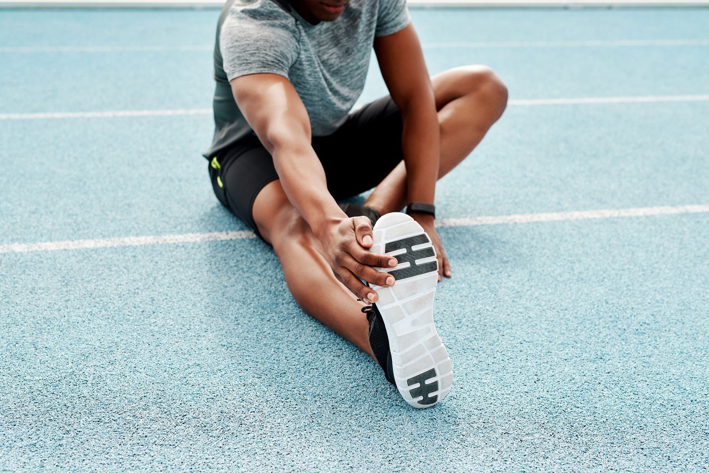 Cropped shot of an unrecognizable athlete sitting alone and stretching before a run on the track