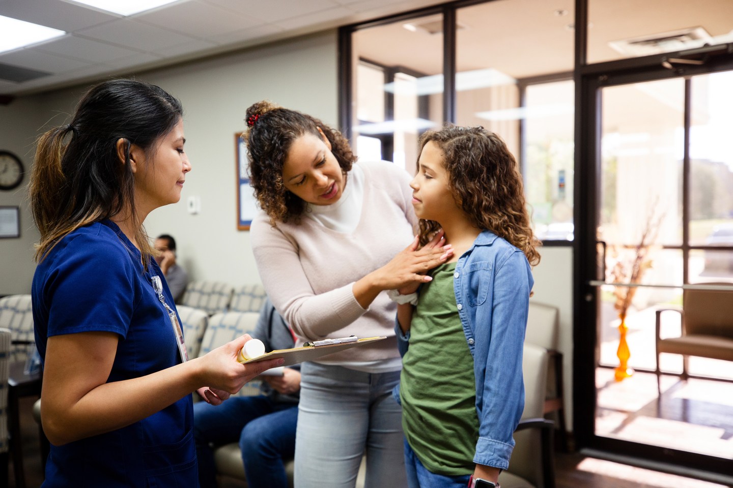 Worried mom discusses her daughter's sore throat and other symptoms with a female nurse in a medical clinic.