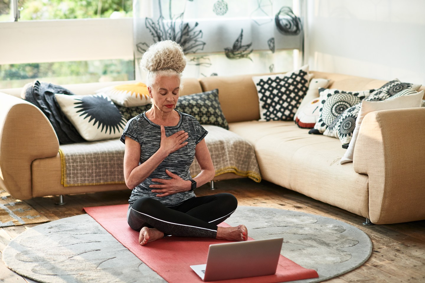 Senior woman with eyes closed meditating, sitting cross-legged on floor.