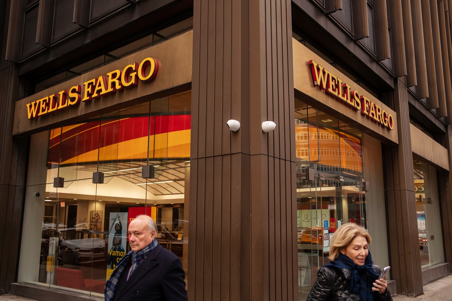 A woman on her phone and a man stand in front of a Wells Fargo bank branch in New York.