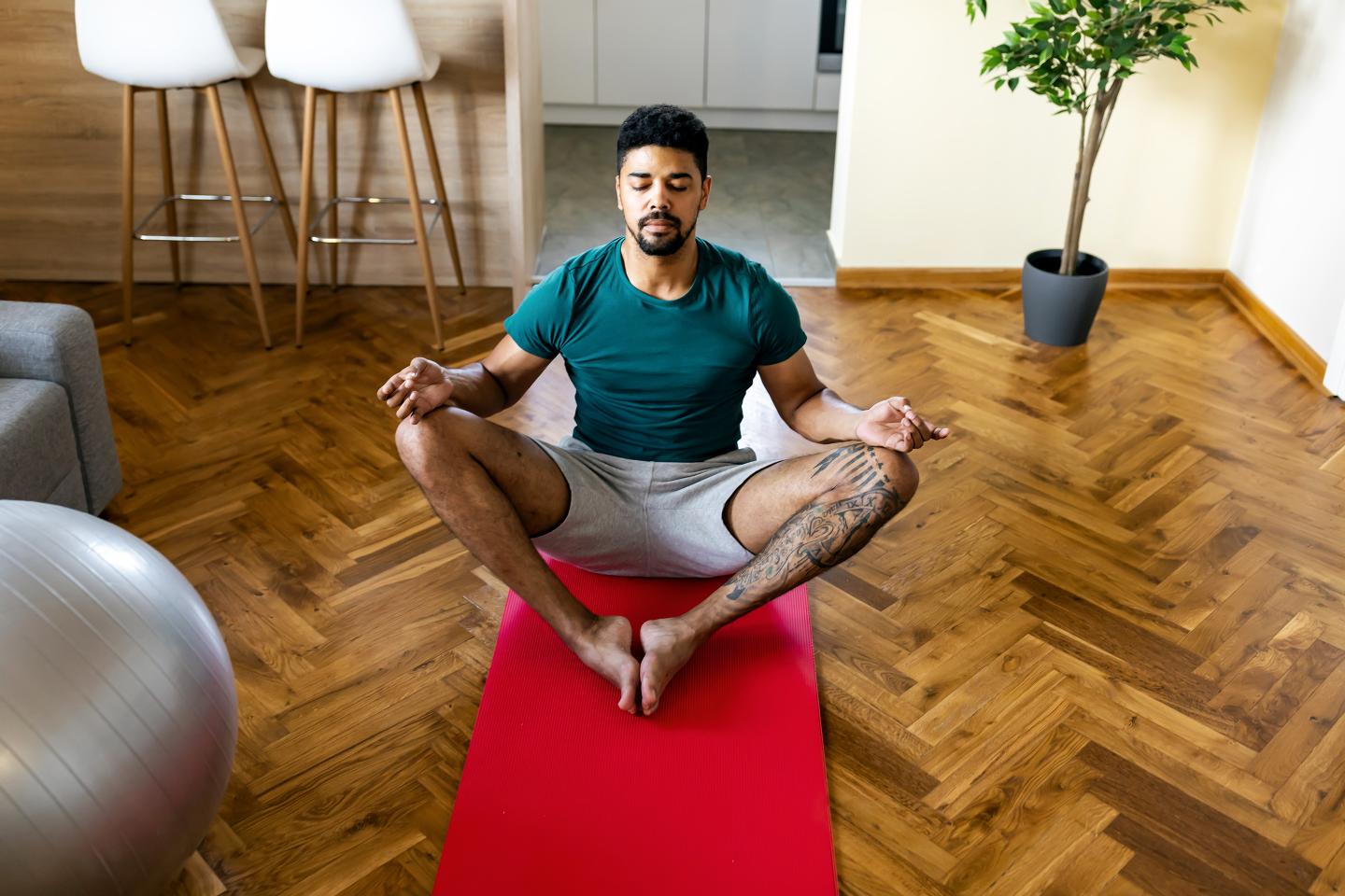 Handsome peaceful young black male sitting cross legged on yoga mat practicing mindful meditation with eyes closed.