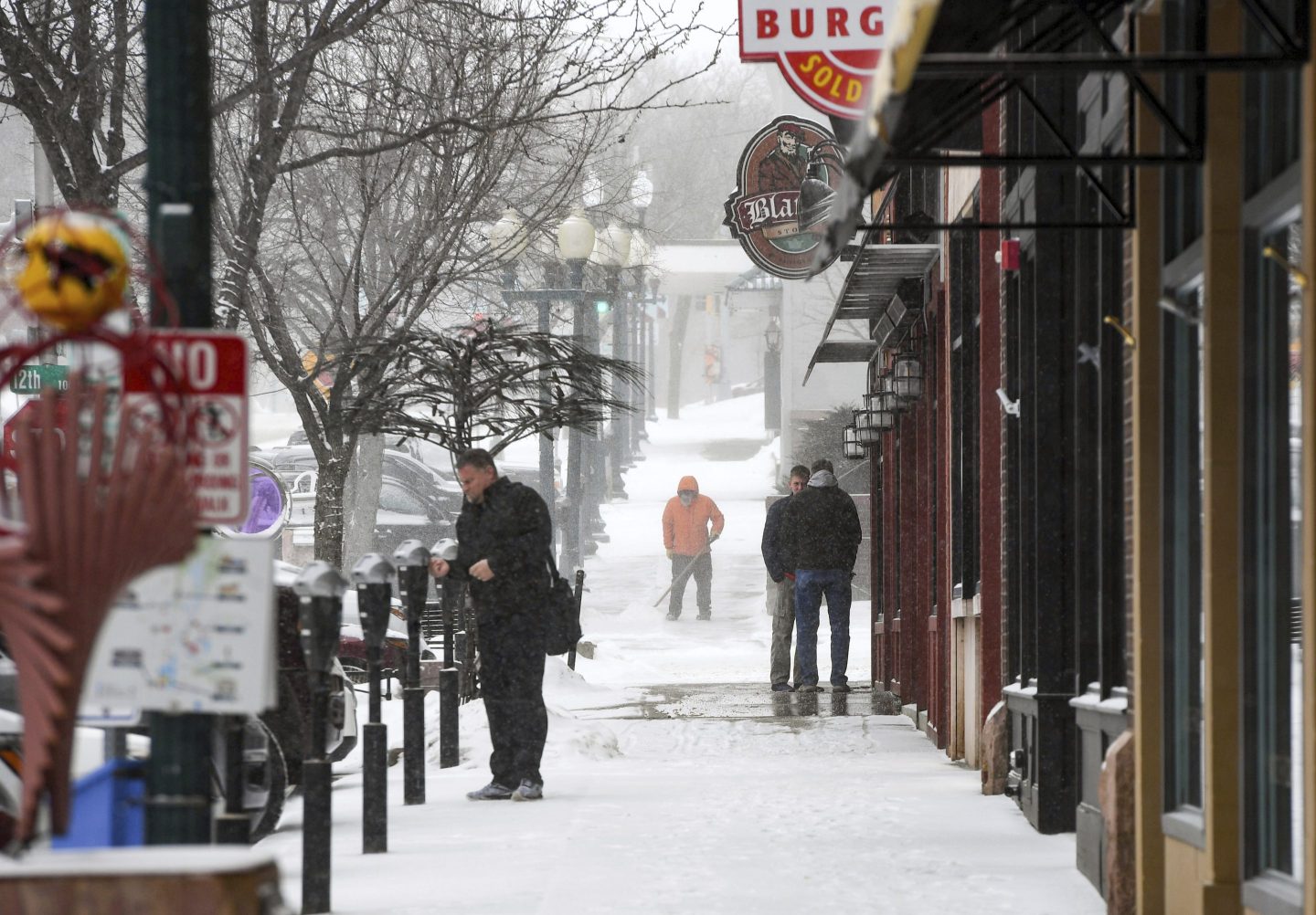 Pedestrians stand as snow falls around them ahead of a winter storm on Feb. 21, 2023, in Sioux Falls, S.D.