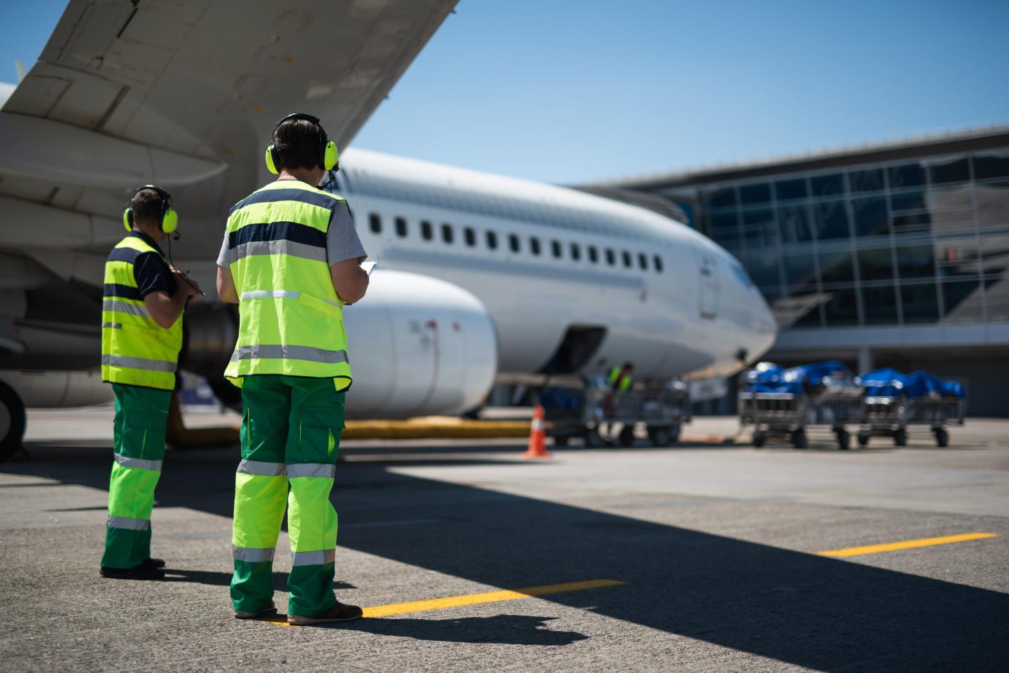 Two airport workers standing next to an aircraft