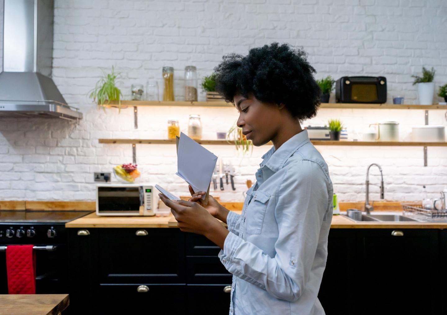 Woman looking through her bills while standing in her kitchen