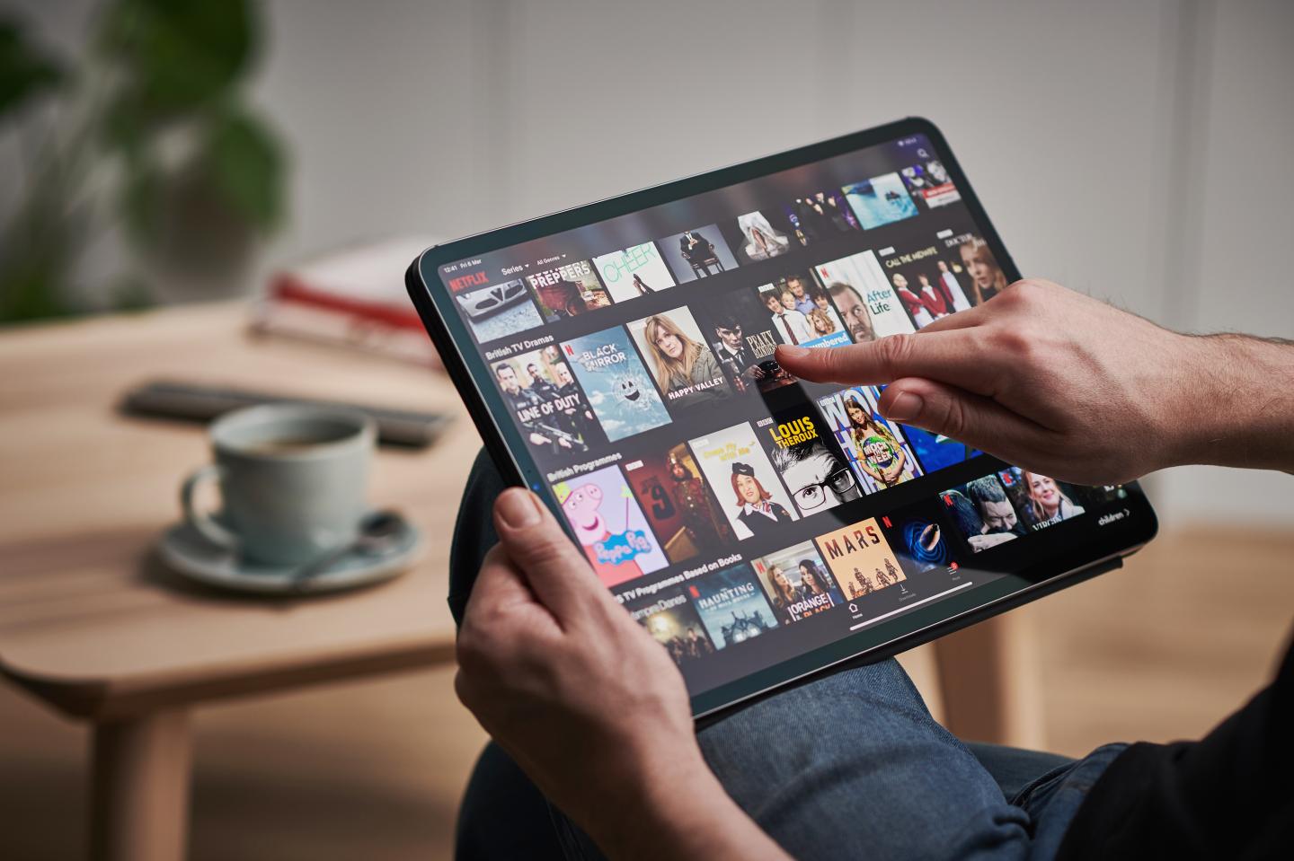 A man is seen scrolling through Netflix on an iPad.