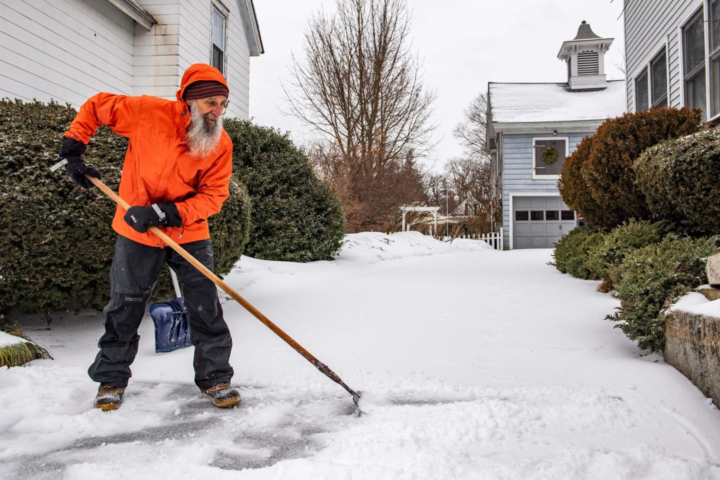 A man breaks up ice and sleet on his driveway during a winter storm in Concord, New Hampshire