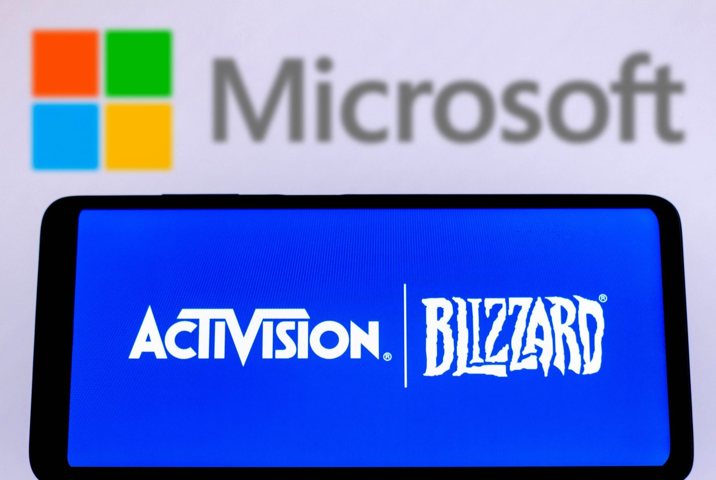 In this photo illustration, Activision Blizzard logo is displayed on a smartphone screen with a Microsoft Corporation logo in the background.