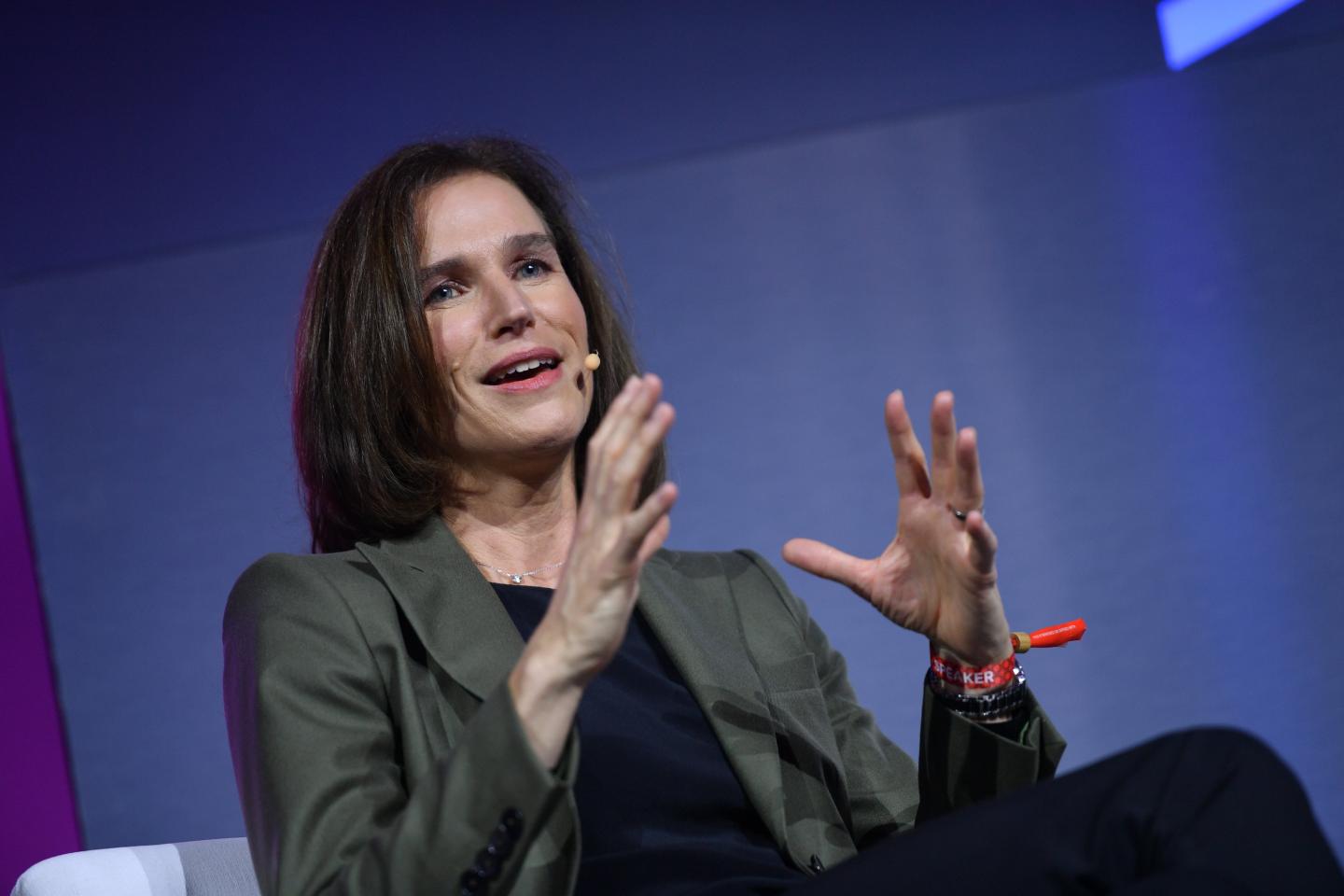 A woman with dark hair in a blazer addresses a crowd