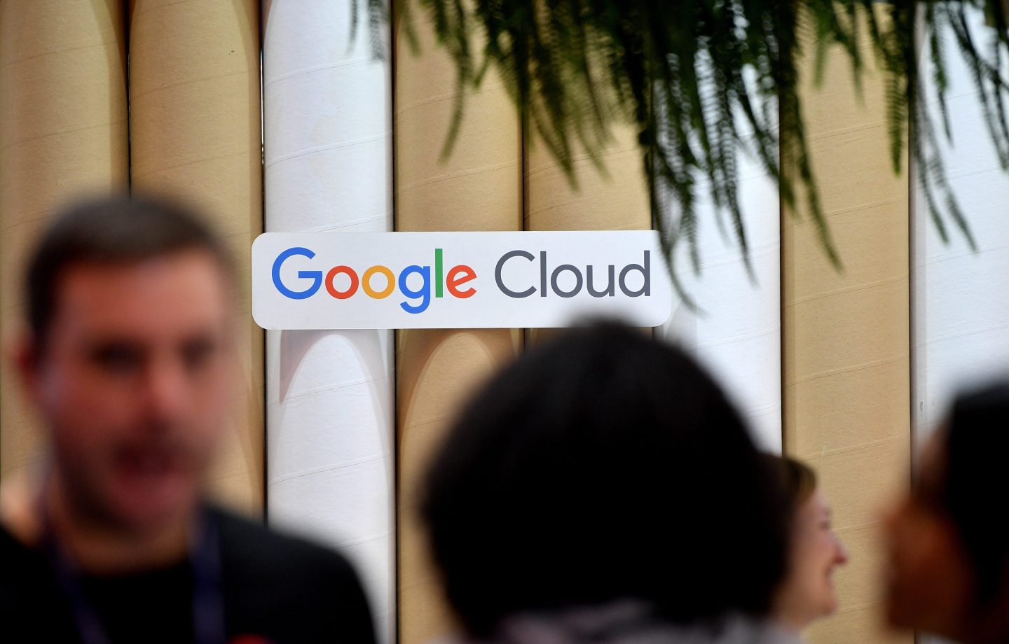 Blurry photos of people as they walk past a Google Cloud sign at a conference.