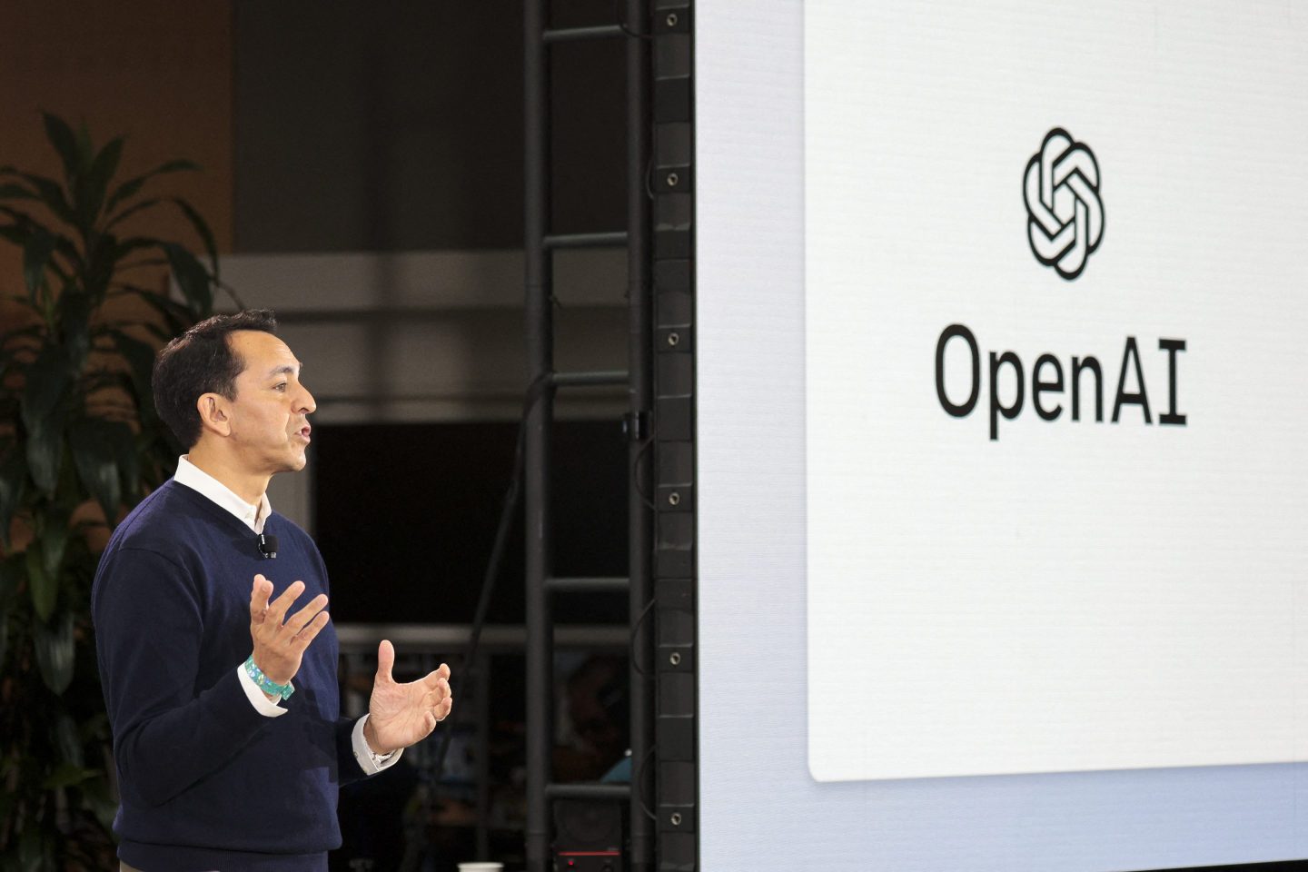 Microsoft executive Yusuf Mehdi next to a presentation showing OpenAI's logo.