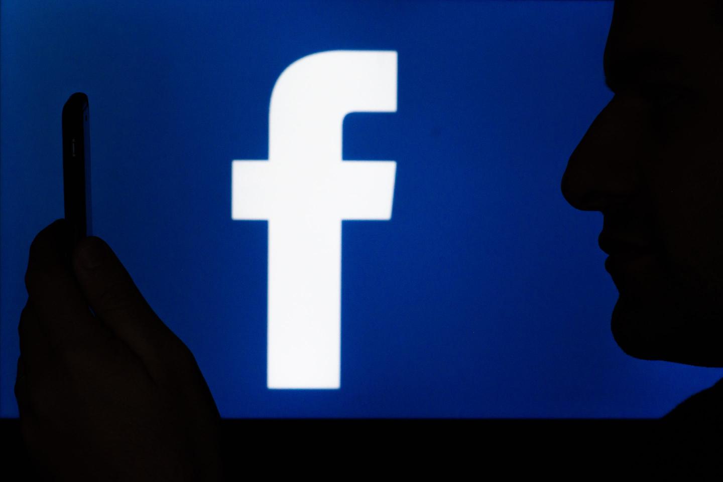 A man holding his phone against the Facebook logo