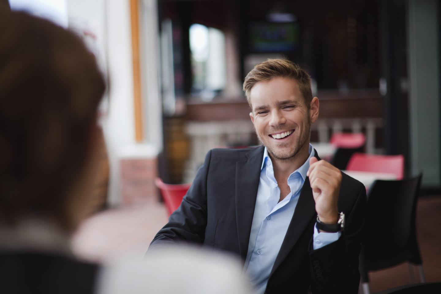 A man in a suit laughs to a colleague