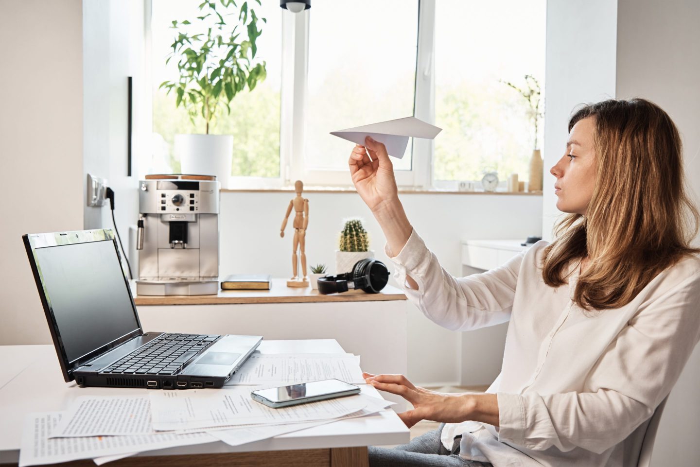 A person holding a paper plane by her work desk