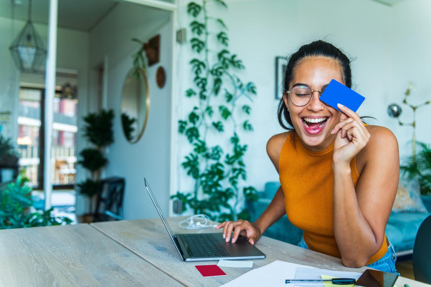 Young woman holding a credit card and smiling while shopping on a laptop