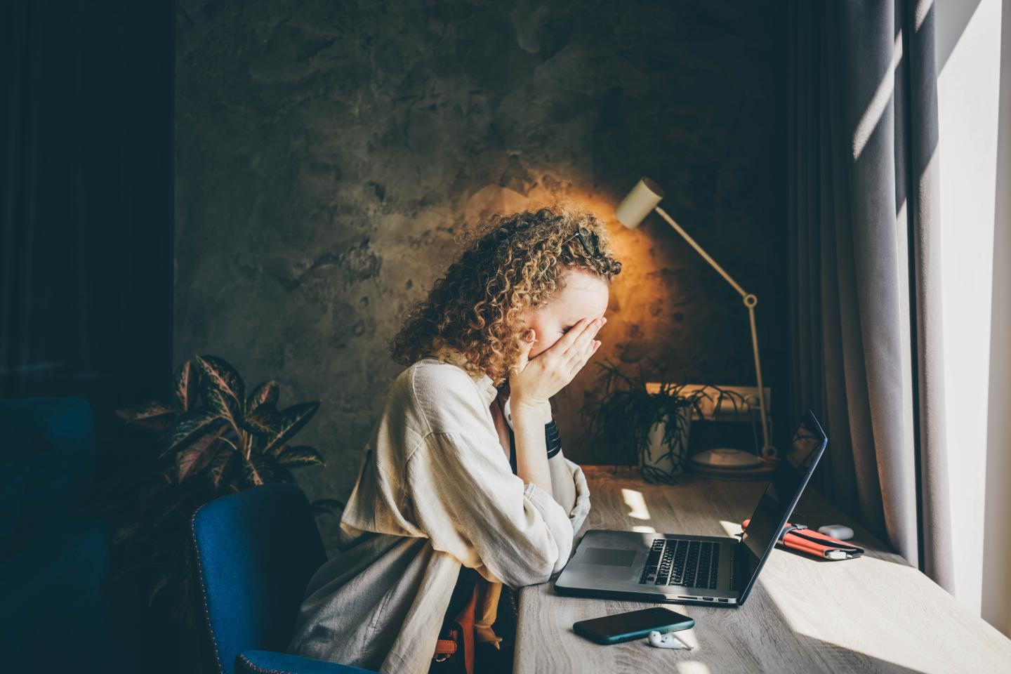 A woman sits at a desk with her head in her hands