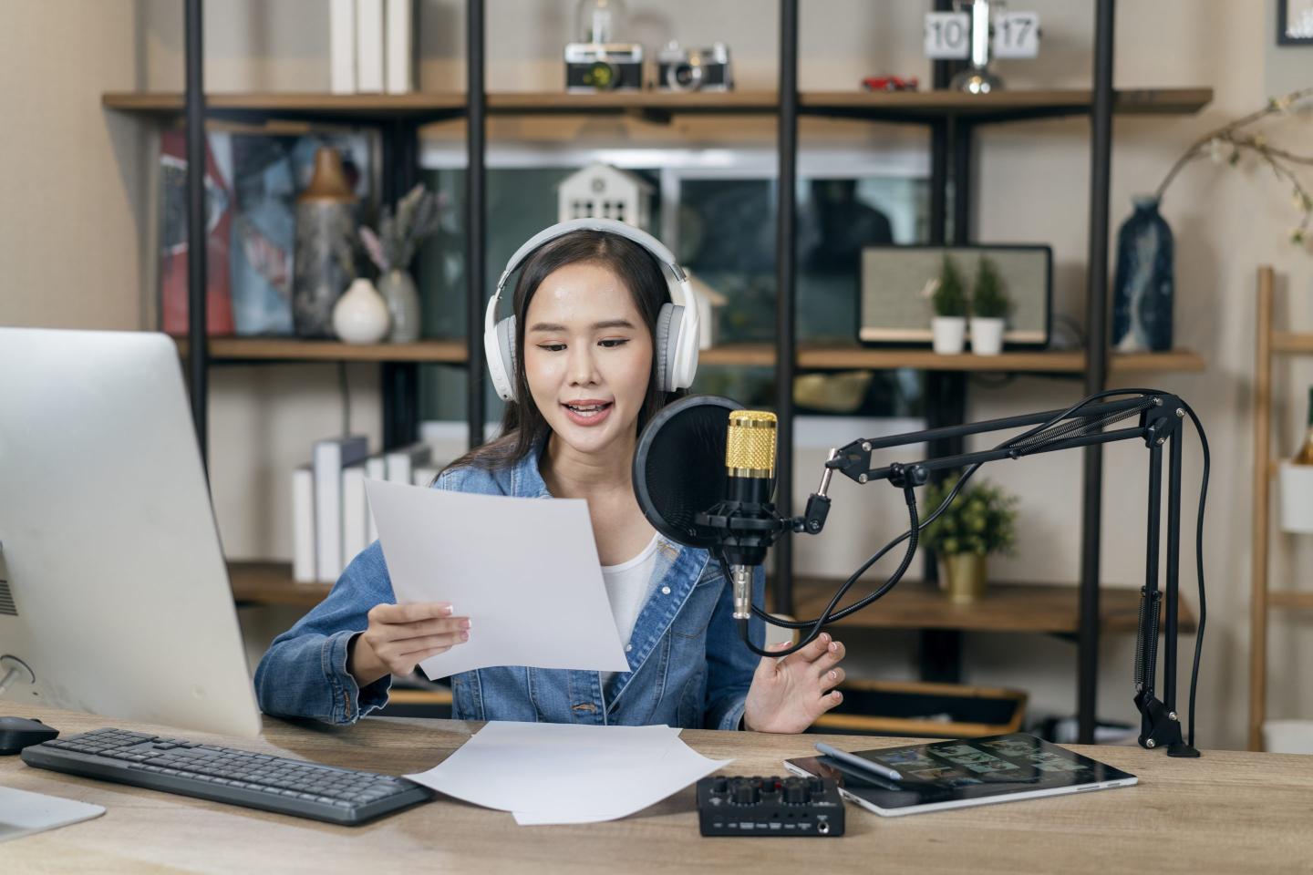 A young woman works on a radio station, talking on a microphone in her home office