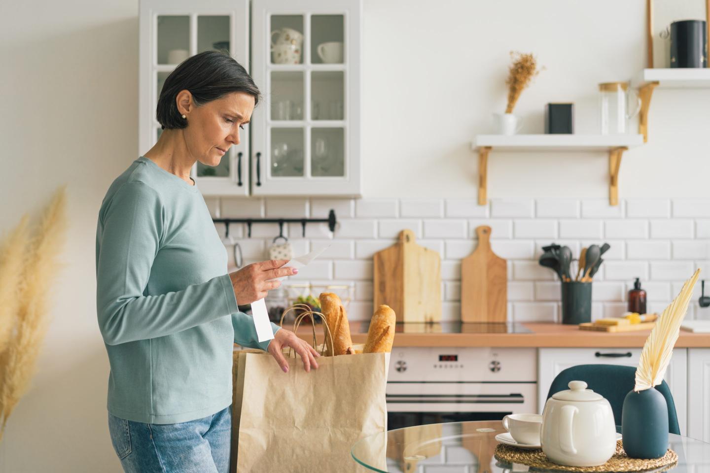 Senior woman frustrated while looking at receipt from grocery store. Rise in price of products concept. Buying consumer goods during inflation. Wisely planning family budget and managing expenses. Facing economic downturn, copy space