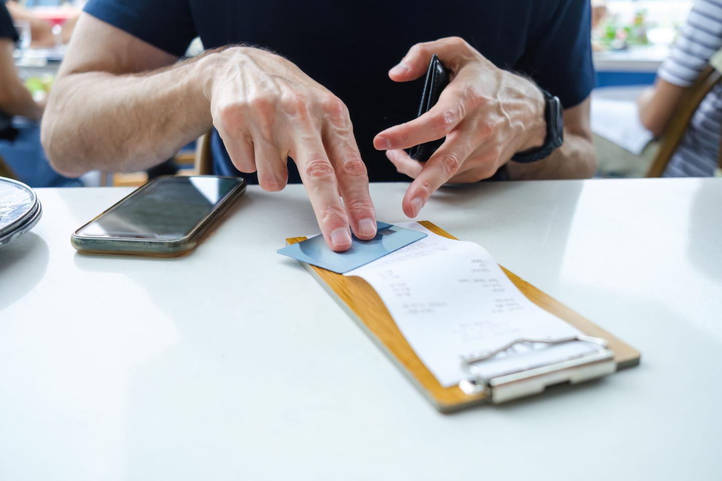 Man placing his credit card on top of bill at restaurant.