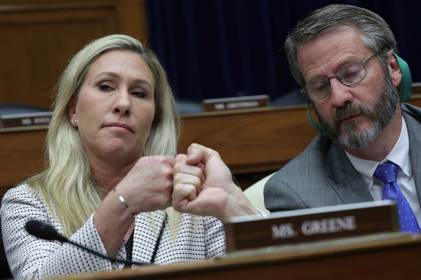 Rep. Marjorie Taylor-Greene (R-Ga.) sitting left fist bumps Rep. Tim Burchett (R-Tenn.) who is sitting next to her behind a blurred-out name plate and microphone.