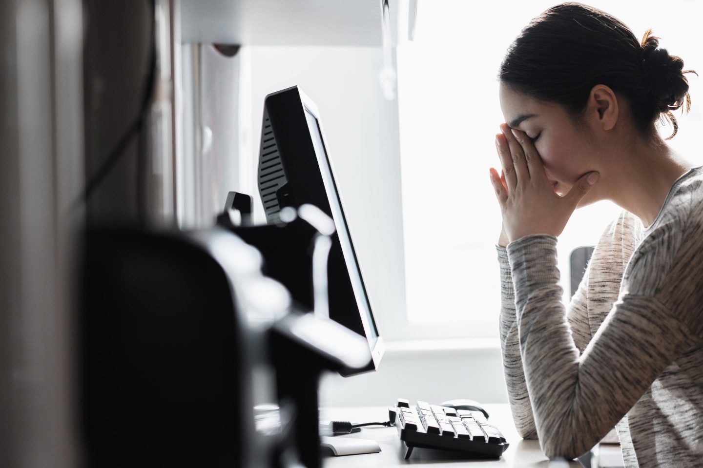 A woman sits at a desk with her head in her hands