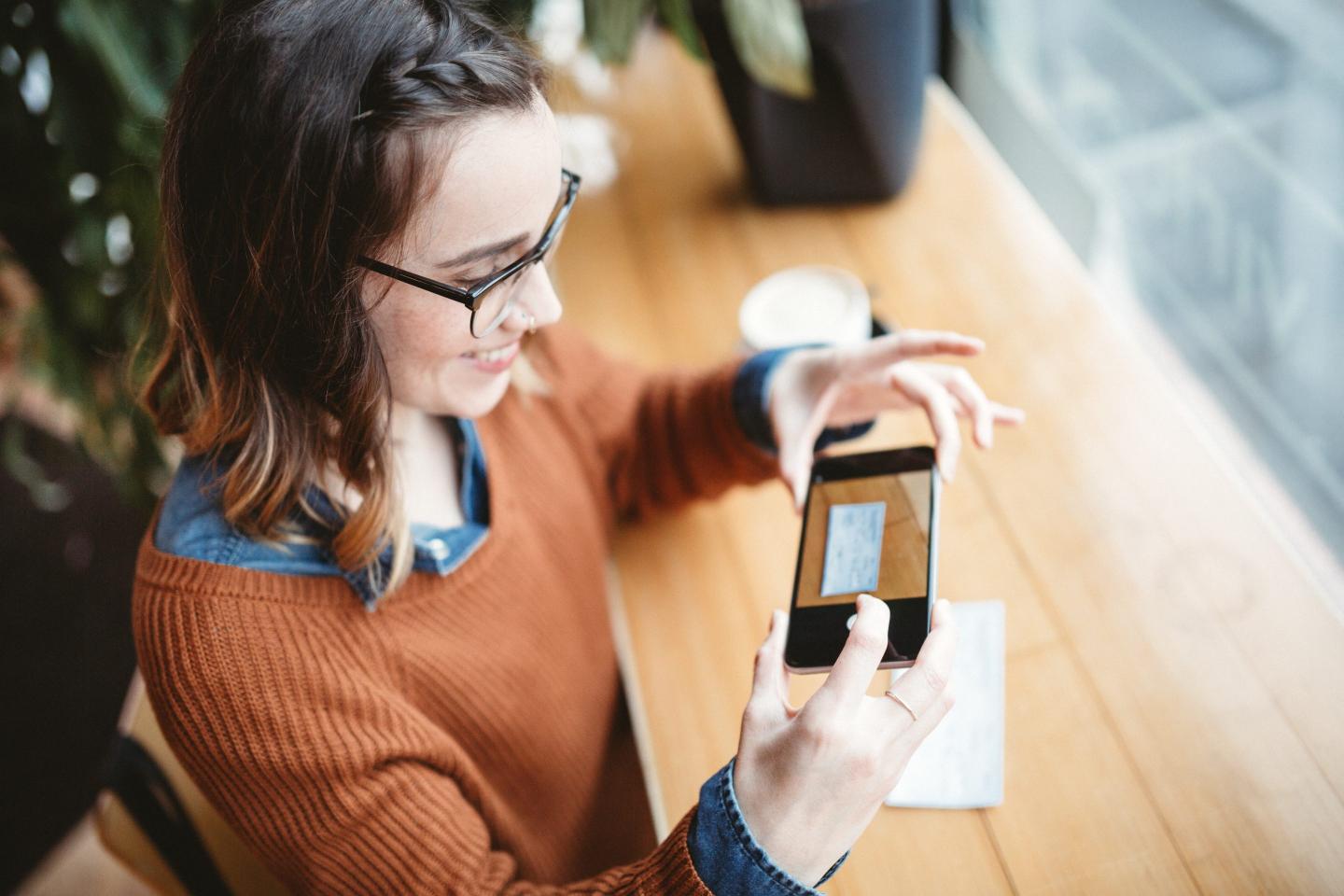 young woman takes a picture with her smart phone of a check or paycheck for digital electronic depositing