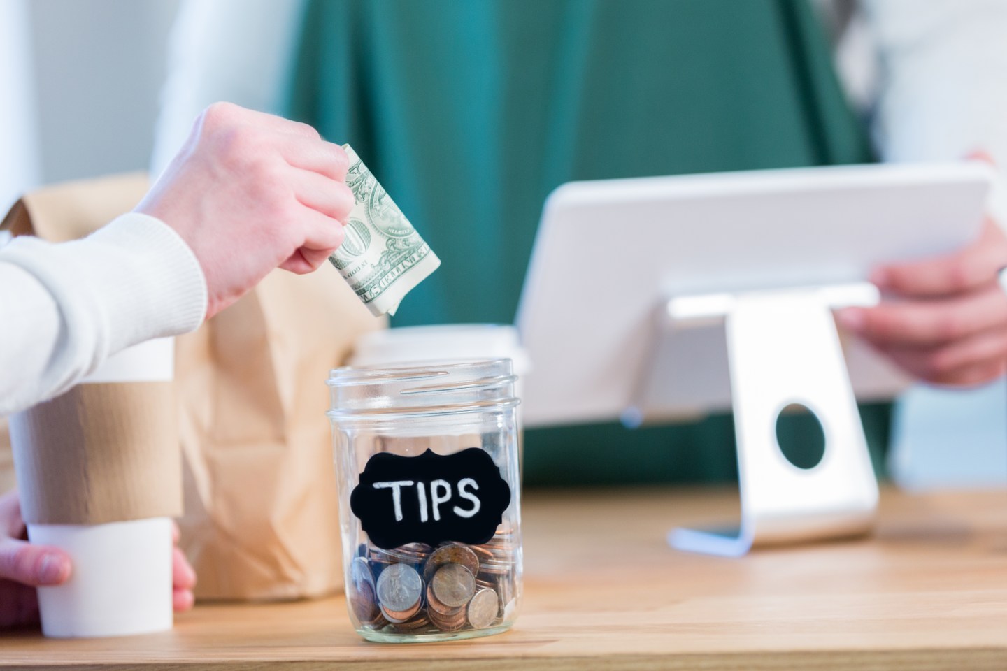 Coffee shop customer puts cash in a tip jar on the counter.