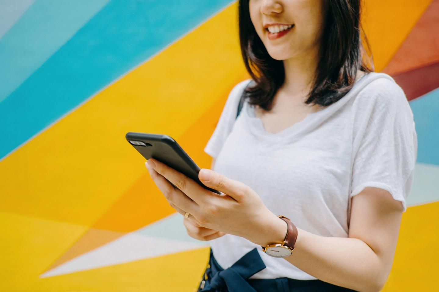 Portrait of smiling young woman using smartphone against colourful background
