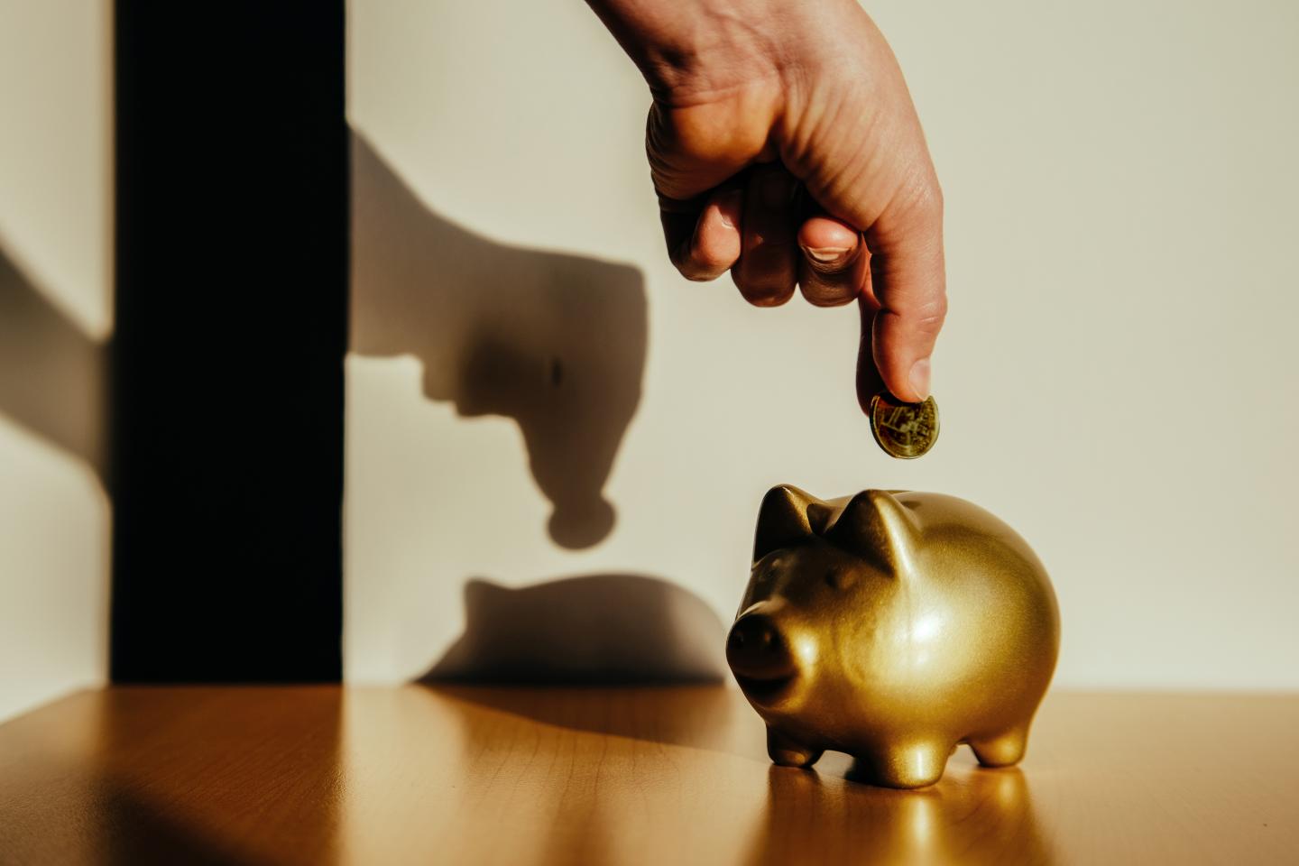 Woman putting a coin in a golden piggy bank in harsh natural light.