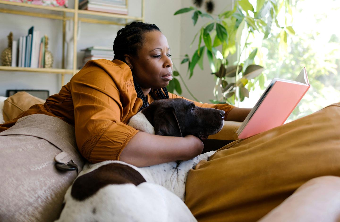 Woman reading book on sofa with her dog